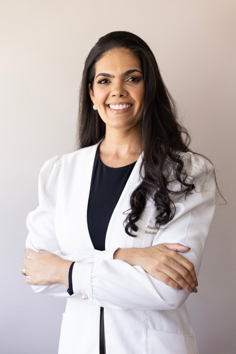 Dra. Andressa Alba, Médica Endocrinologista e Clínica Geral, sorrindo e de braços cruzados.